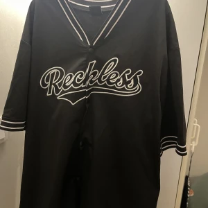 Reckless tröja - Svart Reckless tröja med vitt tryck och knappar. Köpt för 300kr säljer för endast 90kr
