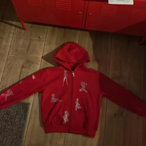 Rhinestone Hoodie röd - Mycket fin och knappt använd röd rhinestone hoodie. Hoodien kommer från thenamedcollective, orginal pris 1250kr. Bra kvalite på materialet och dragkedjan samt rhinestone trycken. Hoodien är i storlek xs/s sitter perfekt. Hoodien är true to size. 