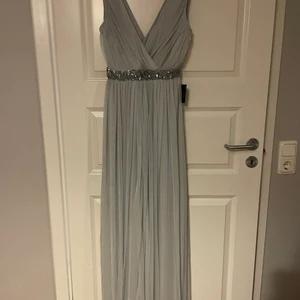 långklänning  - En super fin lång långklänning i gråaktigt färg, i perfekt skick. Perfekt till bal! Aldrig använd och prislappen sitter kvar. Klänningen är i storlek 34 men är lite större i storlek. Kan skicka mer bilder vid intresse av köp!