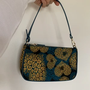 Axelväska  - Axelväska i skimrande turkost/guldigt tyg. Aldrig använd av mig och köpte second hand med original lappar kvar. Jättefint skick. Två innerfack. 