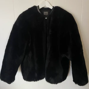 Fluffig jacka - Jacka i fluffig Pälsimitation från Zara, i storlek S. Jackan är varm och har silvriga detajer i kragen och knäpps med dragkedja 