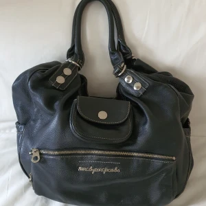 Marc by Marc Jacobs skinnväska - Stor och rymlig skinnväska från Marc by Marc Jacobs. Fin modell med fem småfickor på utsidan och tre på insidan. Mycket bra skick, endast lätt slitage på hörnen. Även helt ren och fräsch inuti.   Mått: 41 cm x 36 cm x 17 cm. Originaldustbag ingår. Äkta! 