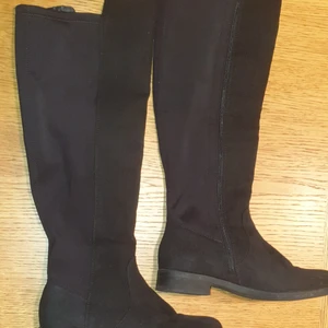 Stretch stövlar strl 36 - Knähöga stövlar i stretch. Fejk mocka framtill och i foten och stretchtyg baktill. Dragkedja. Gummisula, lite räfflad, låg klack. Ofodrade. Obetydlig använda. Köpta på Din Sko. Höjd från häl till kant 42 cm bak, 3 cm högre på framsidan.