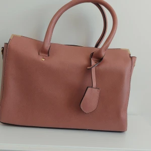 Rosa handväska  - Större rosa handväska. Ett fack med dragkedja och två öppna fack. Kommer även med ett längre axelband. Priset är exklusive fraktavgift.