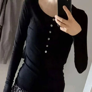 Långärmad topp, stl. S - En svart långärmad topp med dekorativa knappar framtill i stl S. Lite liten i storlek så skulle säga XS-S, lite längre i modellen. Tajt o tunnt tyg men känns inte genomskinlig. Polyester som är mycket elastisk! Köpt på Na-kd. Använd men i nyskick. 