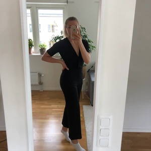 Svart byxdress - Svart byxdress med fickor från Jacqueline de Yong. Mycket stretchigt och lite strukturerat tyg. Djup v-ringning som sitter på plats trots liten byst! Fint skick, endast använd och tvättad 2 ggr. Det finns dock en maska som repats upp några cm på framsidan, men inget som syns på håll