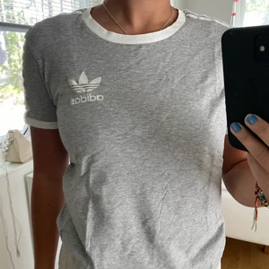 Adidas t-shirt  - Grå t-shirt med adidas tryck och ränder på axlarna 