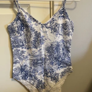 Body - En vit och blå body från H&M med mönster av växter och djur! Bodyn är i bra skick och endast använd en gång. Storlek S