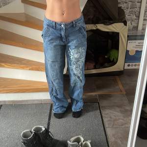 Ett par low waist blåa baggy jeans med tryck på högra  benet från emmiol. E använda och lite sönder gådda i benen/ är 156 cm och pris kan diskuteras