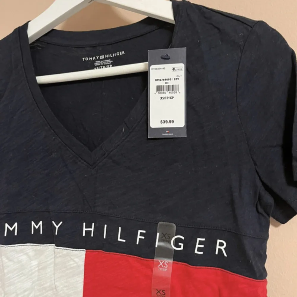 Helt ny T-shirt med V ringning från Tommy Hilfiger, lapparna är kvar på. Storlek XS i färgen vit, röd och marinblå! Nypris 417 kr.. T-shirts.