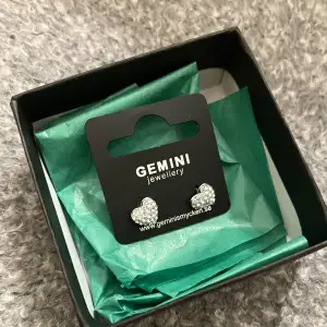 Örhängen från Gemini by Sweden. Hjärtformade med stenar på. Använda en gång bara. Förpackning finns med.