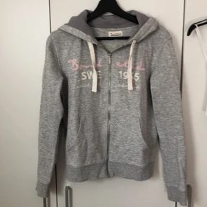 luvtröja / zip-up hoodie från bondelid - Ljusgrå zip-up med rosa och vita broderier. OBS! Den är ljusgrå i verkligheten, ser mörkare ut på bilden. Har använts mycket men är i bra skick. Insidan av luvan har ett extra lager tyg, så luvan är ganska tjock. Kontakta mig gärna vid frågor eller om du är intresserad! Pris kan diskuteras, frakt betalas av köparen.<33