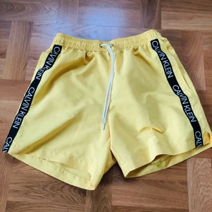 Calvin Klein badshorts - Ett par väldigt fina Calvin Klein badbyxor i Herr Strl S och unik gul färg som är använda  ett par gånger sparsamt. Mycket bra skick, ordentligt tvättade efter varje användning o därav som nya. Sällsynt variant, nypris: 900kr 