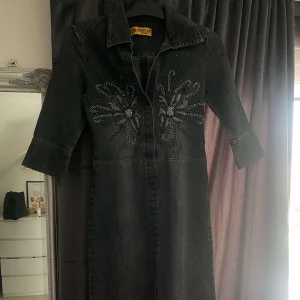 Jeansklänning - Jeansklännikng med trekvarts ärmar och strass. Klänningen går precis över knäna och framhäver figuren på bästa sätt. Det finns knappar så att man kan justera hur öppen eller stängd den ska vara 🫶🏻🥰 