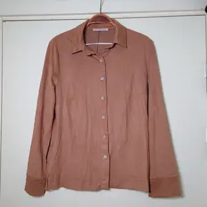 En brun skjorta i speciellt material, känns lite som väldigt tunn mocka (är inte). Ingen storleksmärkning men är som en M🌿