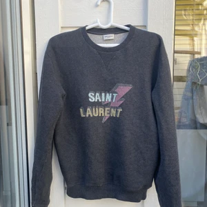 Saint Laurent Lightningbolt Sweatshirt - Säljer nu min Saint Laurent tröja. Snygg tröja som matchar perfekt till ett par ljusblåa jeans. Väldigt fint skick, ända flaw är ett litet hål vid kragen som är igensytt. Dock ingenting man märker av.