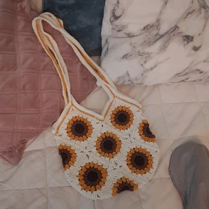 Virkad Väska - Solros - Granny square väska gjord i bomulls och akrylgarn. Väskan är gräddvit med solrosor❣Väskan är ca 28 cm i bredd och ca 30 cm i längd. Axelremmen är ca 75cm lång (Extra lång axelrem) 💕 Perfekt till vår/sommar🌼🌻(Frakt ej inräknad i priset)