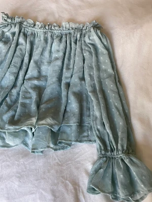 Blus  - Blus från Ginatricot i pastell turkos, kan användas som offshoulder eller vanligt. Prickig med volanger. Aldrig använd, prislapp kvar. Stl 38 men passar bra som mindre stl också. 