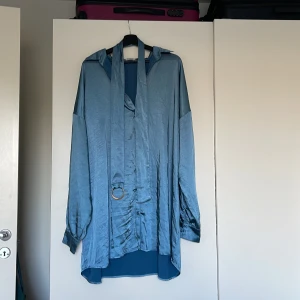 Oversized skjortklänning i satin - Fin Oversized skjortklänning i satin med tillhörande skärp för midjan. Använd en gång och har en mindre fläck på skärpet. 