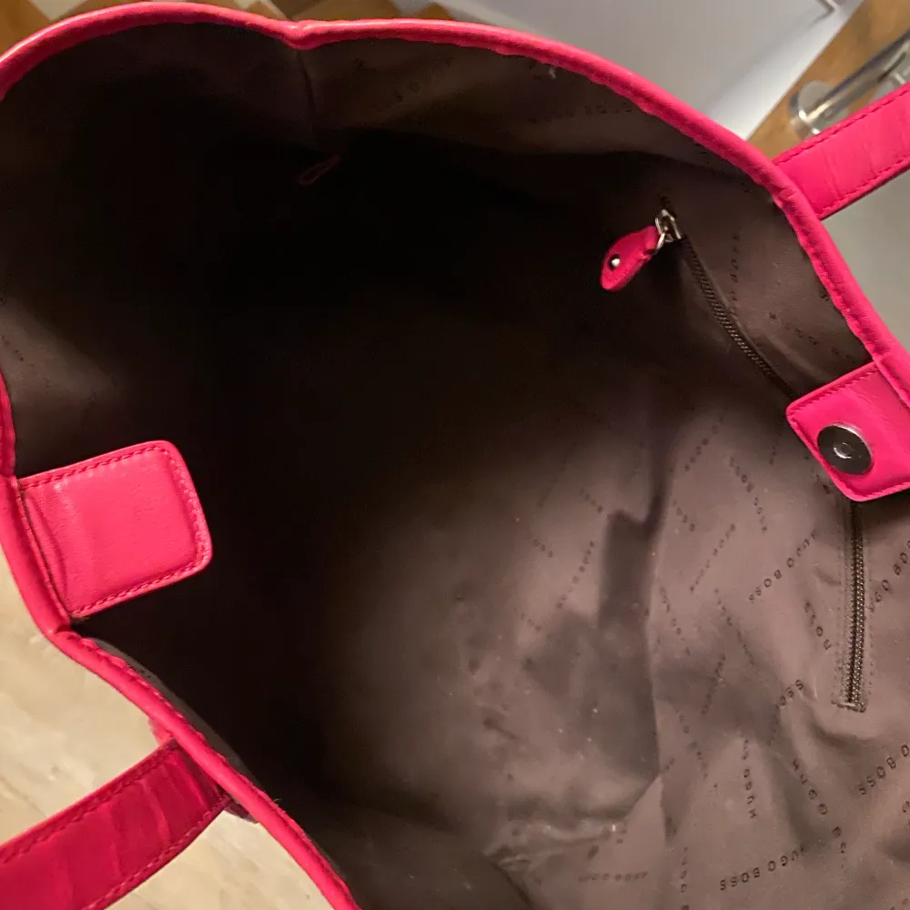 Längd: 43 cm Höjd: 30 cm Bred/djup: 16 cm Säljer en oanvänd Hugo boss väska där även dustbag medföljer. Väskan är köpt i en Hugo Boss butik i Tyskland. Grå med rosa detaljer! 😃 . Väskor.