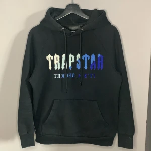 Trapstar hoodie svart - Trapstar hoodie svart med blåvit text, nytt skick                                                                                   Köptes för några veckor sen för 1250;- och säljer eftersom att den inte kom till någon användning då den är för liten