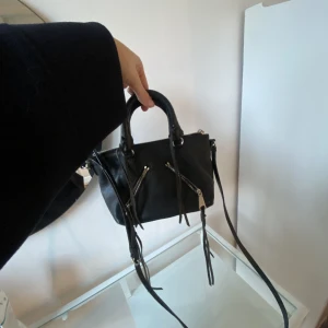Rebecca Minkoff väska - Väska från Rebecca minkoff. Går att hålla i handen eller ha över axeln. Det långa bandet går att justera. Lite dammig på insidan men annars mycket bra skick. 