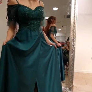 Balklänning - Balklänning i storlek 38 (passar någon med storlek 36 då balklänningar oftast är mindre)  Den är grön med glitter ovantill.  Off-shoulder, golvlång klänning med slits.  Tyget är siden liknande.  Ryggen har grönt genomskinligt tyg i ett rutigt mönster. 