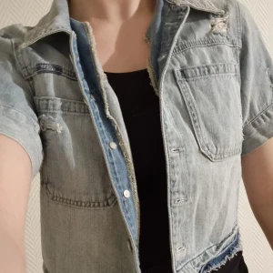 "Trasig" jeansjacka  - "Trasig" kortärmad och kort jeansjacka från guess. Sparsamt använd och fint skick. Säljes pga garderobsrensning.