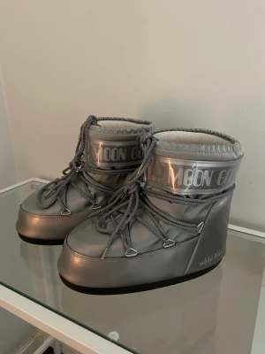 Låga silvriga Moon Boots - Säljer ett par använda men fortsatt användbara Moon Boots. Slitage på hälarna (kan ses på bild 2). Noppriga på insidan. Stolek 39-41. Köpta för 1799kr.