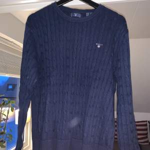Snygg, stilren marinblå kabelstickad tröja från Gant. Den är använd men är fortfarande i väldigt bra skick och har inga som helst skador, 9/10! Storleken är 176, men sitter som S. Nypris: 900kr