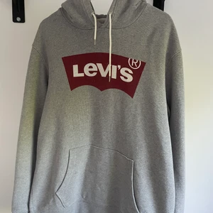 Grå Levis hoodie - Väl använd hoodie från levis, knappt något slitage. Har en fläck på ena sidan längst ner, syns typ inte. Diggar inte trycket längre men annars en go hoodie