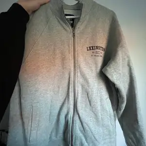 En grå jättefin zip hoodie (utan luva), som har en lite högre krage samt fickor på båda sidor. (herr modell, men passar dam!)