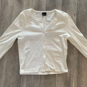 Vit gina topp med knappr - En fin basis tröja från Gina. Man kan ha den knäppt men också använda den som en kofta om det önskas. Den kan vara lite genomskinlig med en mörk bh men den fungerar bra med en vit eller hudfärgad bh. Den har inte kommit till användning alls eller tvättats.💕