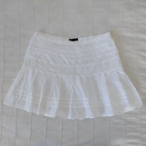 Vit volangkjol med virkade detaljer - Den finaste vita sommarkjolen man kan tänka sig 🤍 Den är i 100% bomull och så fint sydd med virkade detaljer och sidenband. Vitt slätt tyg under. Sparsamt använd och i fint skick (en liten brun prick uppe till vänster och en väldigt svag liten fläck vid det ena virkade bandet - knappt synbart). Dragkedja i vänster sida. Den är inte struken/steamad på bilderna. Storlek 36.