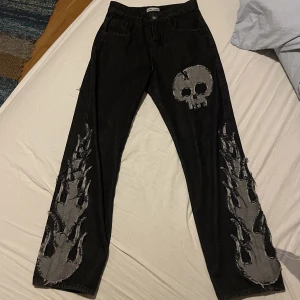 Baggy jeans med döskalle och flammor - As coola baggy jeans med en döskalle flammor och ett kors på från märket Undertrap. Sparsamt använda och inga defekter. Nypris 1600kr 💕