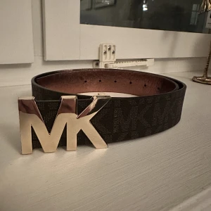 Michael Kors bälte - Bälte ifrån Michael Kors i Strl M (100cm) med logga i guld. Knappt använt så säljes i fint skick. Kasse medföljer 