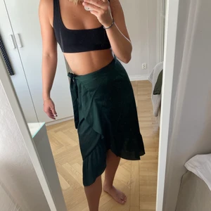 Omlottkjol från Neo Noir - Säljer denna snygga mörkgröna omlottakjol från neo noir. Den har en liten volang längst ner och band man knyter i midjan. Den kommer inte till användning längre och säljer därför vidare den. Frakt tillkommer om inget annat är överenskommet ☺️