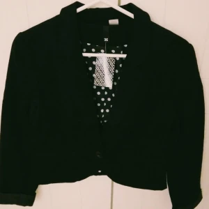 Helt NY & OANVÄND svart kort kavaj med prickigt foder. Storlek: 36/SMALL. Felfri - Helt NY & OANVÄND snygg svart kort kavaj med svart och vit prickigt foder. Stängs med knapp och har 2 små fickor fram. Storlek: 36/SMALL. Felfri/inga defekter. Lappar/tags sitter kvar sedan inköpet.