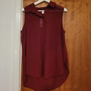 Ärmlös skjorta/blus - Aldrig använd, prislapp finns kvar. Lite genomskinlig, men fin. Längd framsida - ca. 63cm Längd baksida - ca 72 cm Axelbredd - ca 35 cm