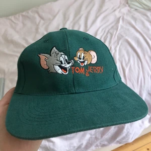 Keps - Grön Tom & Jerry keps med reglerbar storlek men eftersom jag har en så gigantisk hjärna är den för liten för mig. Inga defekter! Skriv för fler bilder eller vid frågor!!b