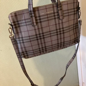 Laptopväska/handväska Don Donna - Rutig väska från Don Donna.  Färger: grå och rosa.  Väldigt fint skick.  Perfekt storlek till skolböcker, laptop, iPad mm. Passar bra till skolan/ jobbet lr bara en snygg detalj till din outfit.  B: 36cm. H: 27cm. D: 4cm Axelrem ingår.  Rök-/djurfritt hem