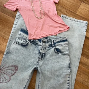 Ljusblå jeans med fjärilsdetaljer - Snygga ljusblå jeans med stentvättad look och glittriga fjärilar i strass på benet och bakfickan. Modellen har raka ben och klassisk femficksdesign. Perfekta för dig som vill sticka ut lite extra med coola detaljer. Bilderna tagna från hon som sålde dom innan men hon har godkänt att jag får ta bilderna igen!