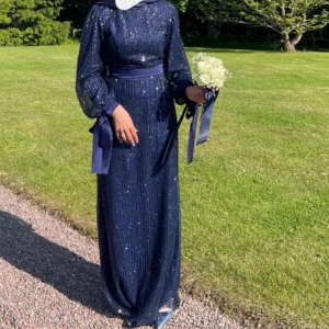 Marinblå glittrig långklänning med rosetter - Säljer en marinblå långklänning med glittrigt mönster och markerad midja. Klänningen har långa puffärmar med breda rosetter vid handlederna och ett matchande midjeband. Perfekt för dig som vill sticka ut med stil och elegans. Användes endast en gång ”tre timmar” Storkek 38 passar en 36