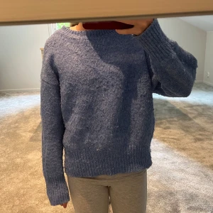 Blå stickad tröja med lång ärm - Mysig blå stickad tröja med rund hals och långa ärmar. Tröjan har en loose passform och ribbade muddar vid ärmslut och nederkant. Perfekt för att hålla sig varm under kyliga dagar.