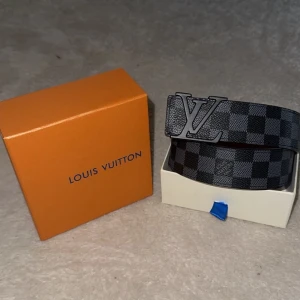 Svart och grått bälte - Snyggt svart och grått bälte med rutigt mönster. Bältet har en klassisk design och kommer i en exklusiv förpackning. Perfekt accessoar för att lyfta din outfit med en modern touch.