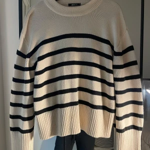 Randig beige stickad tröja Gina Tricot - Säljer en beige stickad tröja från Gina Tricot med svarta horisontella ränder. Tröjan har en loose passform, bred ribbad mudd vid ärmslut och nederkant samt rund halsringning. Perfekt för lager-på-lager under hösten och vintern.
