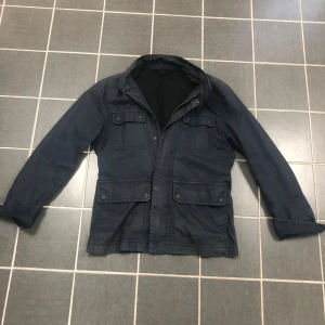 Mörkblå field jacket Tiger of Sweden - Snygg mörkblå jacka från Tiger of Sweden. Stilren design som funkar till många outfits. !Passar mellan 177-185! Har ett litet slitage/hål (se bild 5) inget man ser vid andvändning.Pris är ej hugget i sten🤩