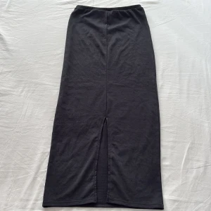Svart långkjol med slits från H&M - Svart långkjol från H&M i mjuk bomullskvalitet. Kjolen har en rak passform och en snygg slits bak som ger extra rörelsefrihet. Perfekt att styla med sneakers eller boots för en chill look.
