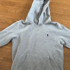 Grå hoodie från Polo Ralph Lauren - Säljer en stilren grå hoodie från Polo Ralph Lauren med klassisk huva och magficka. Tröjan har lång ärm och en liten broderad logga på bröstet. Perfekt för dig som gillar enkel och tidlös streetstyle. Pris kan diskuteras 
