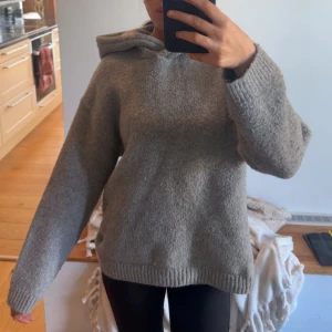 Grå stickad hoodie med huva - Mysig grå stickad hoodie med oversized passform och stora ribbade muddar. Tröjan har en rejäl huva och är perfekt för kyliga dagar. Enkel och stilren design som passar till allt. Säljes då jag rensar garderoben!